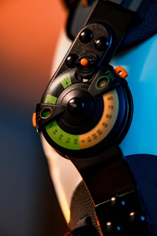 Close-up of a black gaming headset with colorful controls including green and orange circular dials and buttons, lit against blue and orange background